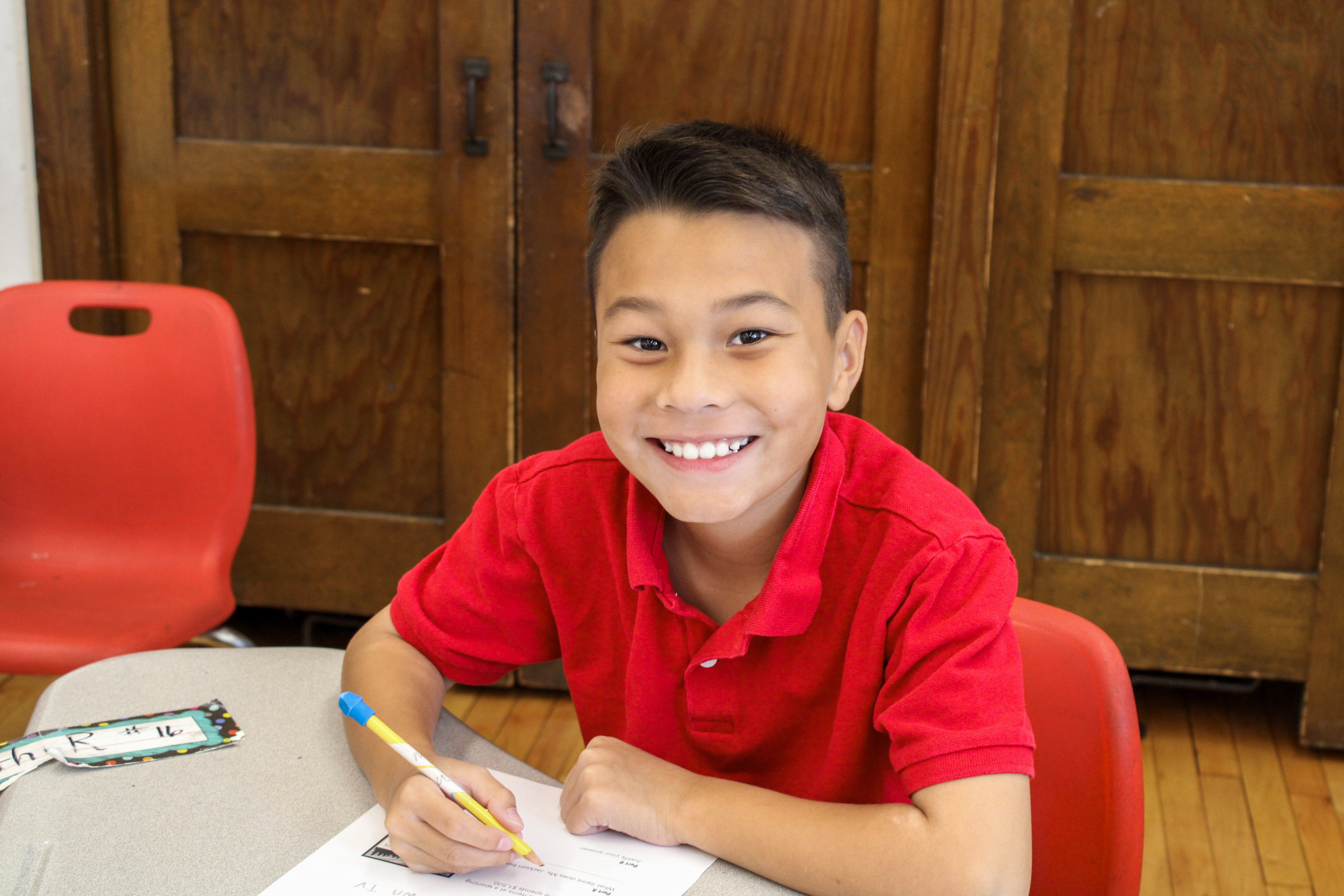 Young student smiling at camera with pencil and paper on desk